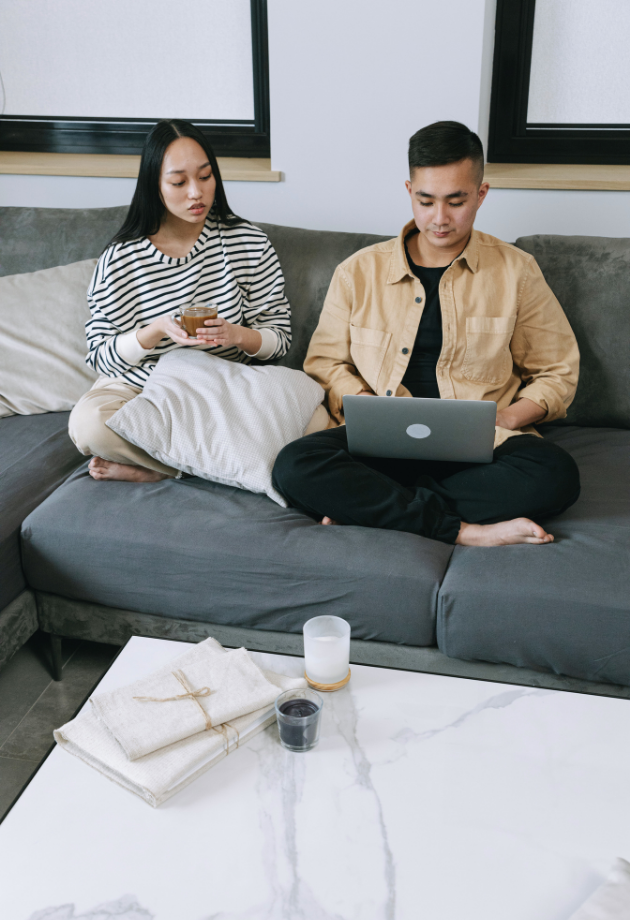 man and woman sitting on couch looking at laptop